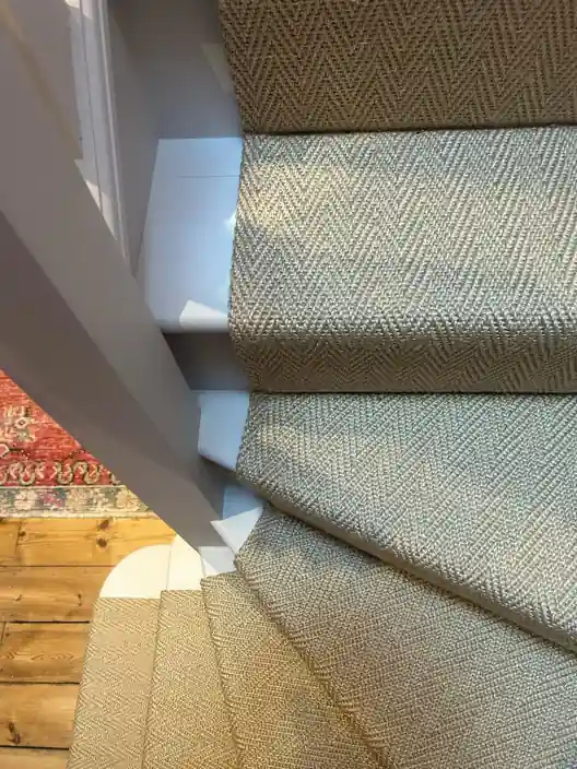 Beige herringbone stair runner on winding white steps.