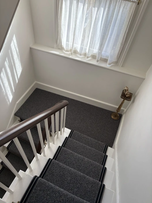 Striped stair runner with white walls and wood rail.